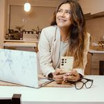 Happy woman holding phone in a modern kitchen setting, illustrating a casual lifestyle.