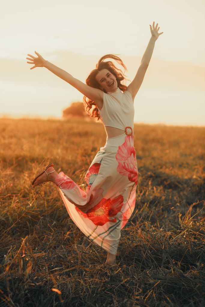 Happy woman in a floral dress leaping joyfully in a sunlit field at sunset.
