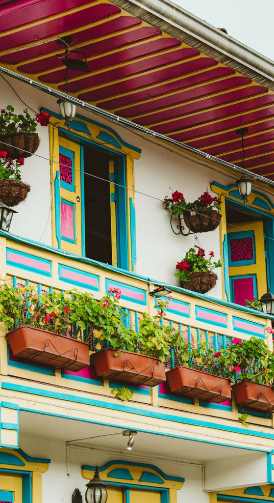 Vibrant facade with a traditional balcony adorned with colorful potted plants.